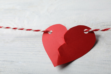 Broken red paper heart and rope on white wooden table, closeup. Relationship problems concept