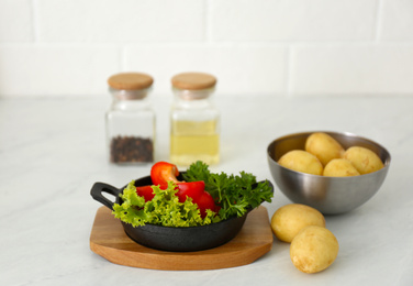 Raw potatoes and portioned frying pan with products on table
