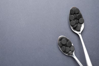 Activated charcoal pills in spoons on grey background, flat lay with space for text. Potent sorbent