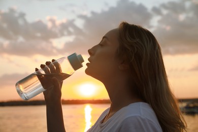Young woman drinking water to prevent heat stroke near river at sunset