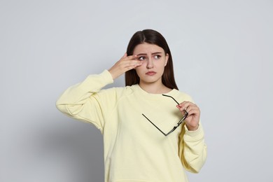 Young woman suffering from eyestrain on light background