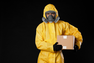 Man wearing chemical protective suit with cardboard box on black background. Prevention of virus spread