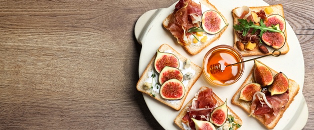 Photo of Sandwiches with figs, proscuitto and cheese on wooden table, top view. Space for text