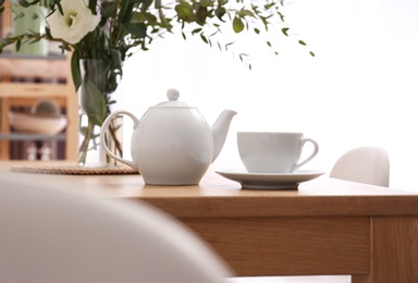 Teapot, cup and flowers on wooden dining table indoors. Kitchen interior