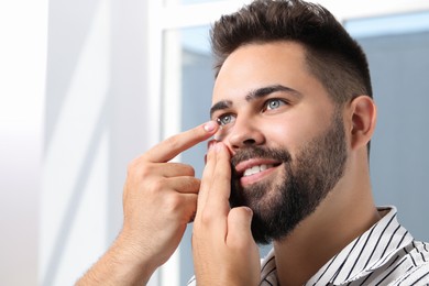 Young man putting in contact lens indoors