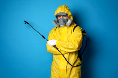 Man wearing protective suit with insecticide sprayer on blue background. Pest control