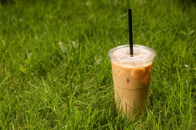 Photo of Takeaway plastic cup with cold coffee drink and straw on green grass outdoors, space for text