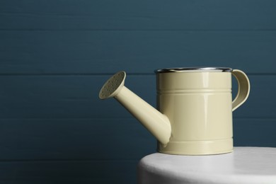 Photo of Beige metal watering can on table against blue wooden background, space for text