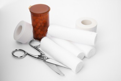 Photo of Medical bandage rolls, pills, sticking plaster and scissors on white background