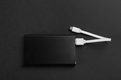 Modern portable charger with cable on black background, top view