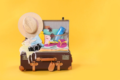 Packed vintage suitcase with different beach objects on orange background, space for text. Summer vacation