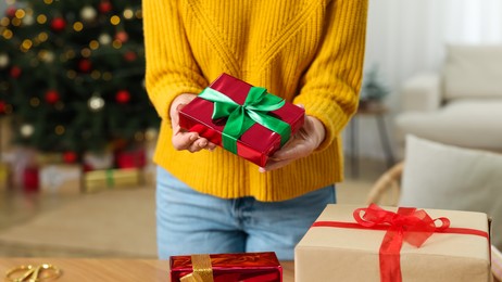 Woman with beautifully wrapped Christmas gifts indoors, closeup