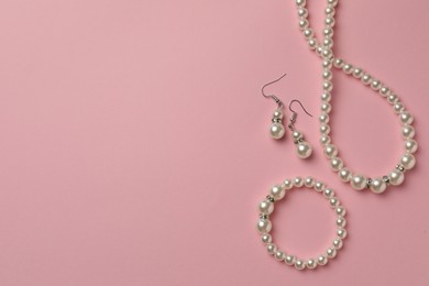 Elegant necklace, bracelet and earrings with pearls on pink background, flat lay. Space for text