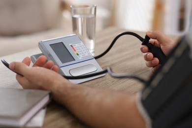 Man checking blood pressure at wooden table indoors, closeup