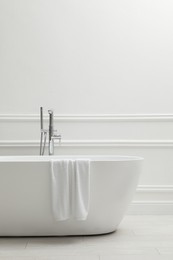 Modern ceramic bathtub with towel near white wall indoors