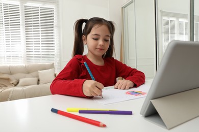Little girl drawing on paper with pencil at online lesson indoors. Distance learning