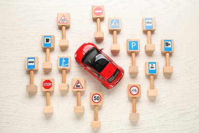 Many different miniature road signs and car on white wooden table, flat lay. Driving school