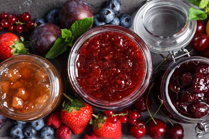 Photo of Jars with different jams and fresh fruits on grey table, flat lay