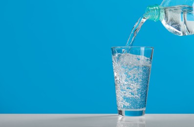 Pouring soda water from bottle into glass on light blue background, space for text