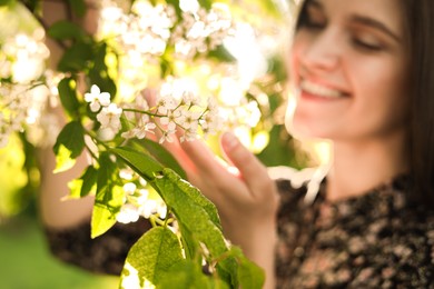 Beautiful young woman near blossoming tree in park, focus on flowers