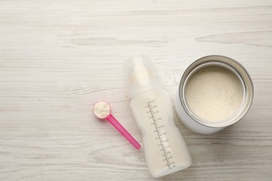 Feeding bottle with infant formula and powder on white wooden table, flat lay. Space for text