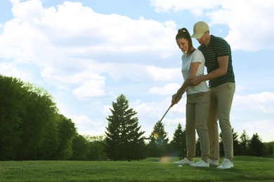 Man teaching his girlfriend to play golf on green course