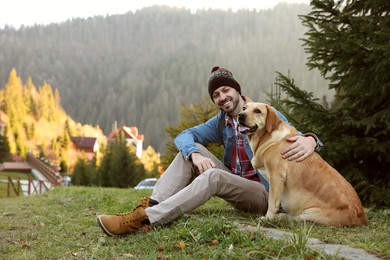 Happy man and adorable dog sitting on green grass in mountains. Traveling with pet