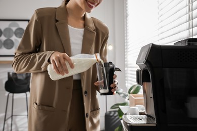 Photo of Young woman pouring milk into container near modern coffee machine in office, closeup