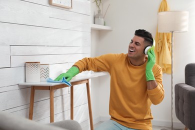 Man in headphones with rag singing while cleaning at home