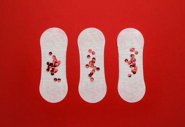Sanitary pads with sequins on red background, flat lay. Menstrual cycle