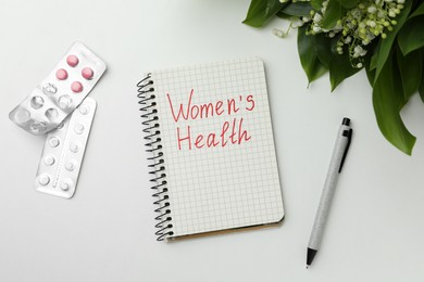 Notebook with text Women's Health and pills on white table, flat lay