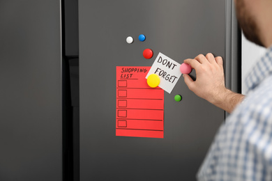 Man putting shopping list and reminder on refrigerator door, closeup