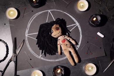 Female voodoo doll pierced with pins and ceremonial items on grey table, flat lay