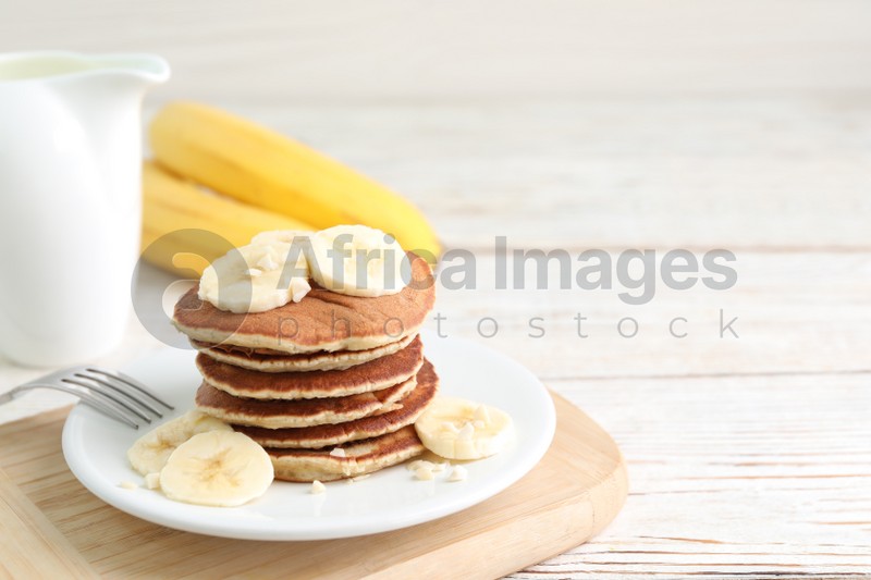Photo of Plate of banana pancakes served on white wooden table. Space for text