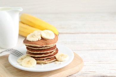 Plate of banana pancakes served on white wooden table. Space for text