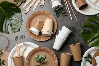 Flat lay composition with disposable tableware and different green leaves on grey background