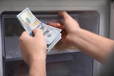 Man hiding money in refrigerator, closeup. Financial savings