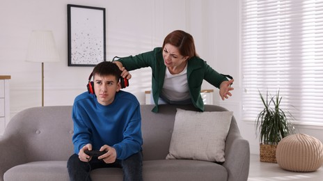 Mother scolding her son while he playing videogame at home. Teenager problems
