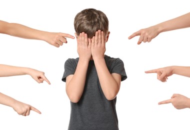 Photo of Boy covering face with hands and kids pointing at him on white background. Children's bullying