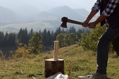 Man with axe cutting firewood on hill, closeup