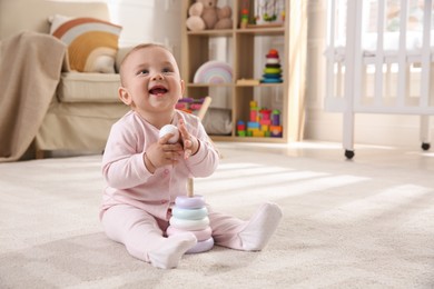 Cute baby girl playing with toy pyramid on floor at home