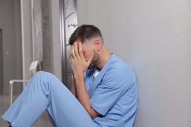 Photo of Exhausted doctor near grey wall in hospital corridor