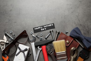 Card with phrase HAPPY FATHER'S DAY, different tools and male accessories on grey background, flat lay. Space for text