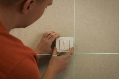 Man using cross line laser level for installation of light switch in plasterboard