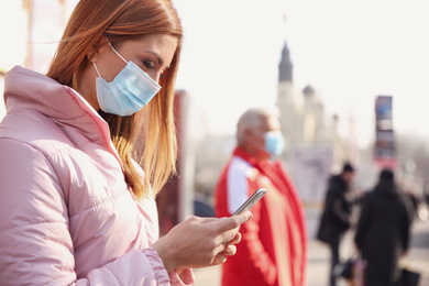 Woman with medical mask and mobile phone on city street. Virus protection