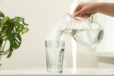 Photo of Woman pouring water from jug into glass on white table indoors, closeup