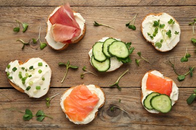 Photo of Delicious sandwiches with cream cheese and other ingredients on wooden table, flat lay