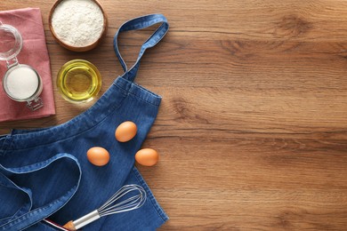 Photo of Denim apron with kitchen tool and different ingredients on wooden table, flat lay. Space for text