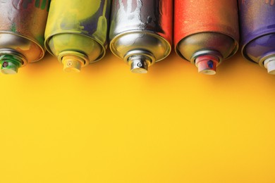 Used cans of spray paints on yellow background, space for text. Graffiti supplies