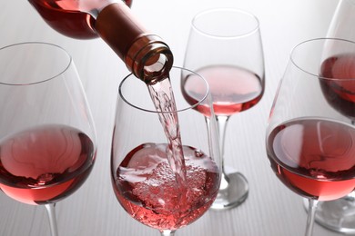 Photo of Pouring rose wine from bottle into glasses on wooden table, closeup